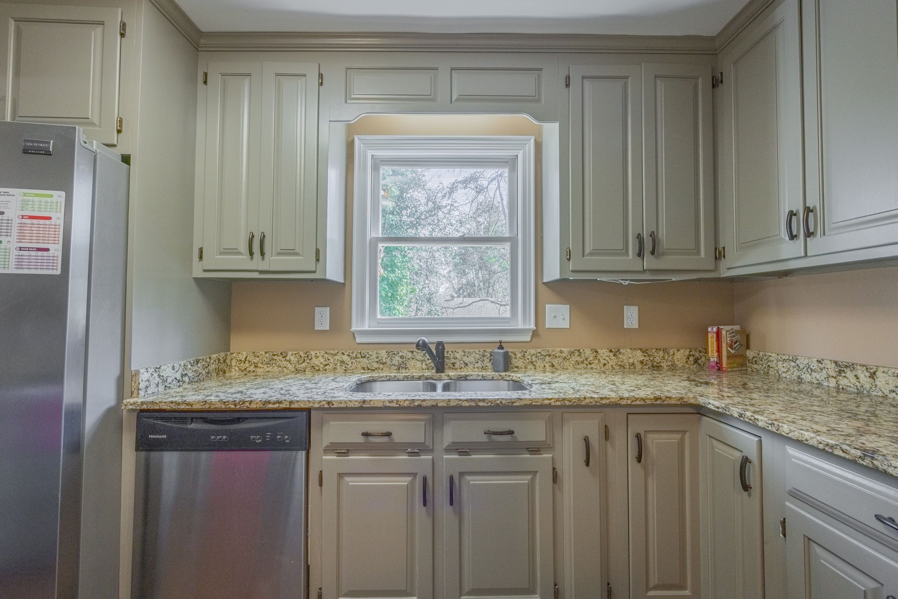 A kitchen with light-colored cabinets, a granite countertop, a stainless steel refrigerator, and a dishwasher.