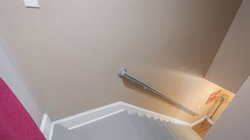 A staircase with a metal handrail, a white wall with a light switch, and a wooden floor.