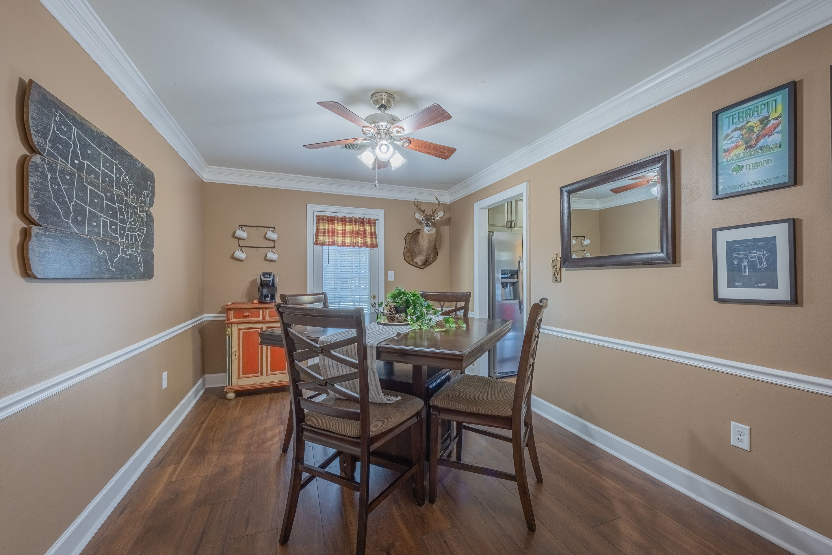 A dining area with a wooden table, four chairs, a ceiling fan, and a wall-mounted map.