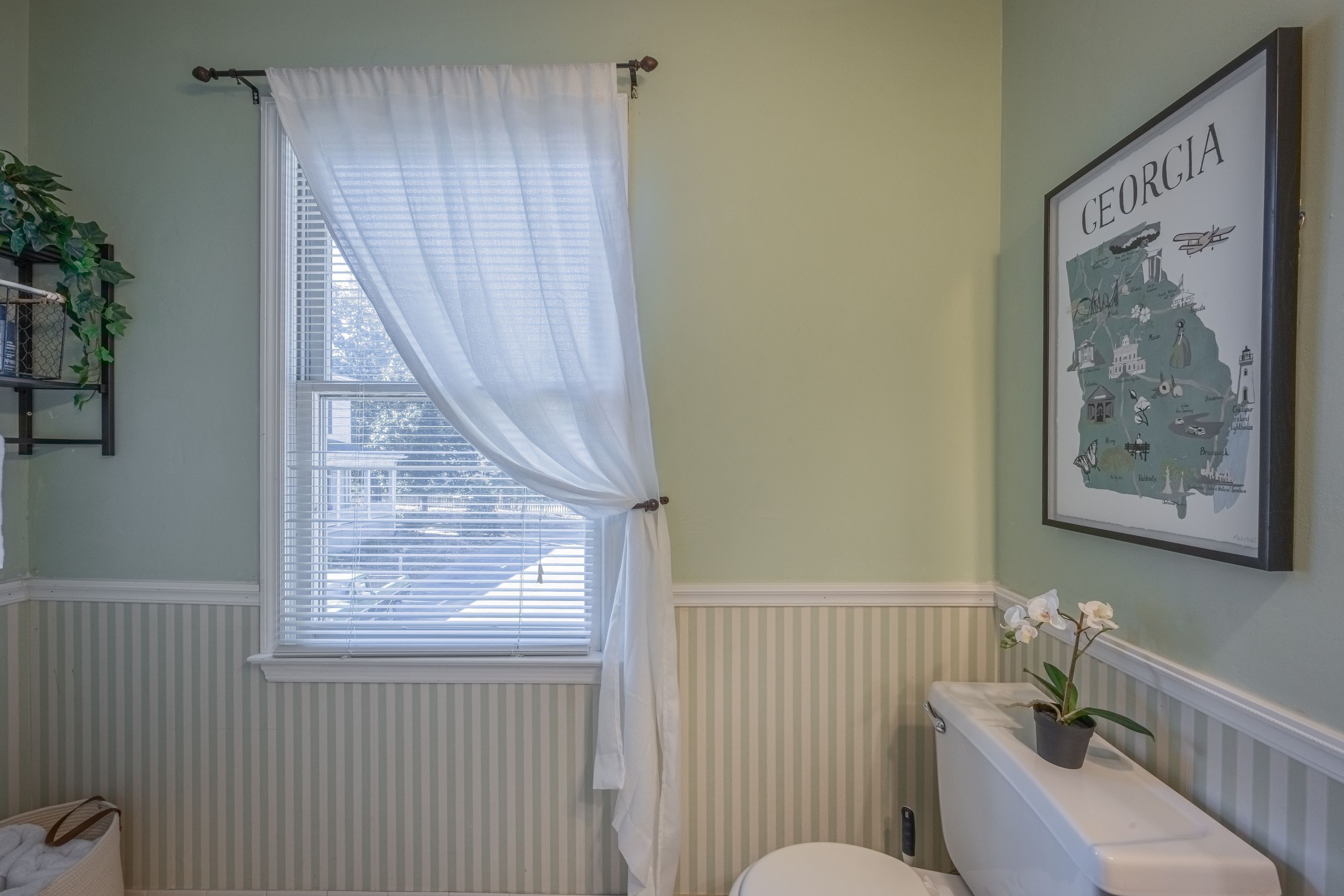 A bathroom with a window, a toilet, a radiator, and a framed map of Georgia on the wall.
