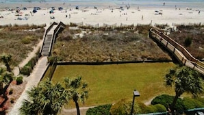 A beach with a wooden boardwalk leading to a grassy area with palm trees. - Beach Lover's Condo With Spectacular Ocean View, Pool, Lazy River, & Jacuzzi!  (North Myrtle Beach)