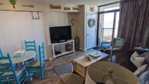 A living room with a TV, a dining table with chairs, a sofa, and a large lamp. - Beach Lover's Condo With Spectacular Ocean View, Pool, Lazy River, & Jacuzzi!  (North Myrtle Beach)