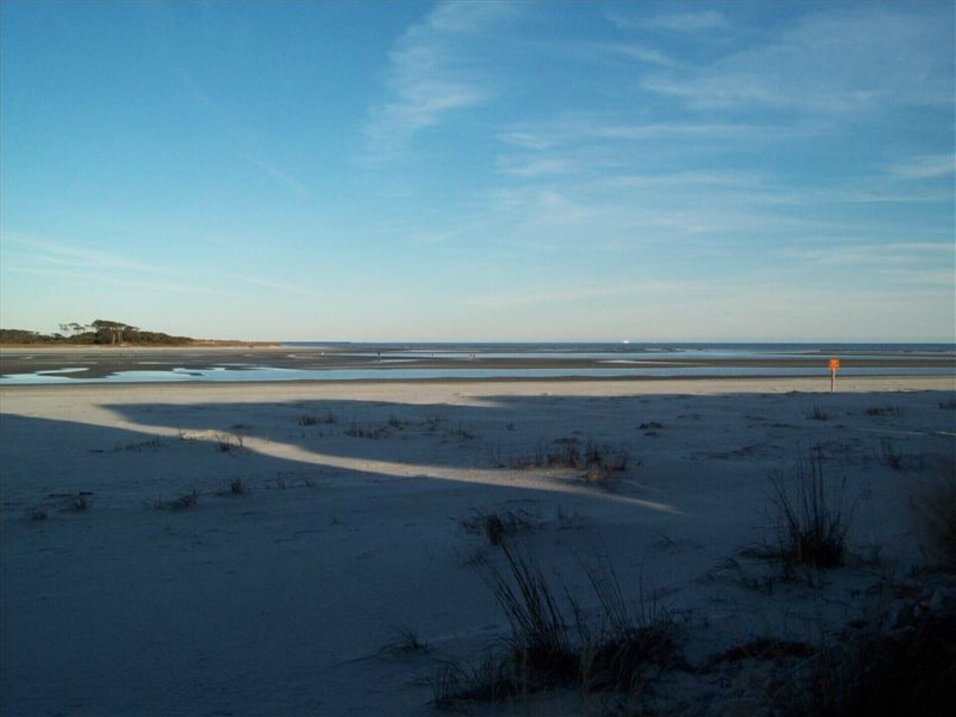 A beach with sand dunes, a clear sky, and a distant shoreline.