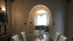 A dining room with a long table, six chairs, a chandelier, and a piano in the background. - Stunning Mediterranean Monument Avenue flat in the heart of RVA's Fan District (Richmond)