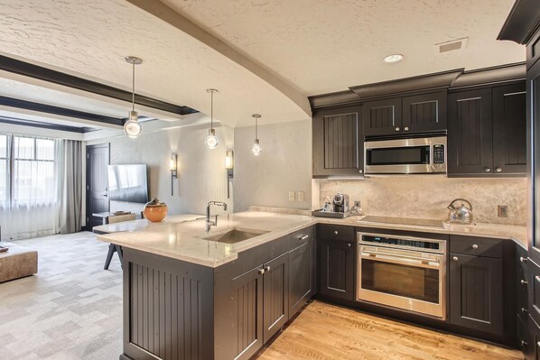 Une cuisine moderne avec des meubles de couleur sombre, des appareils en acier inoxydable et des luminaires suspendus.
