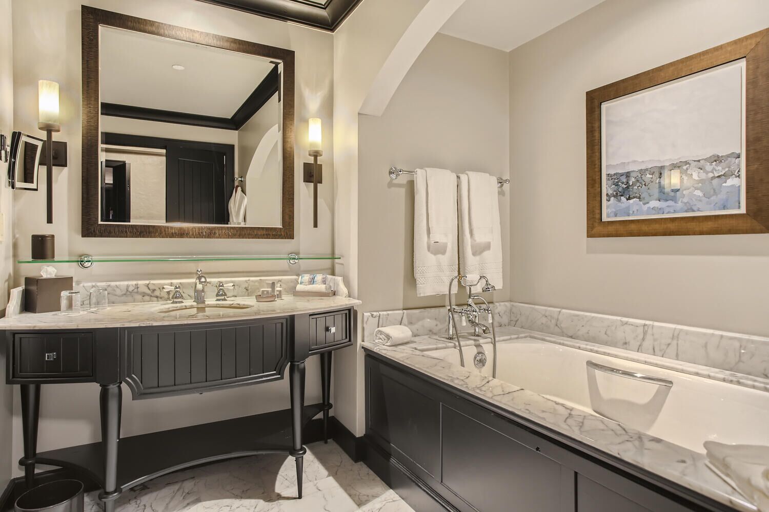 A modern bathroom with a dual sink vanity, a large mirror, a bathtub, and a framed painting on the wall.