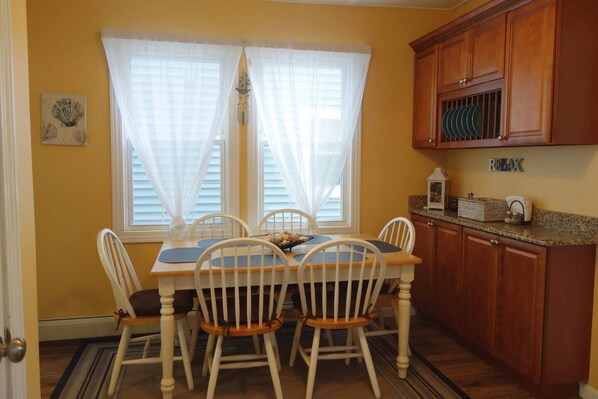 A dining area with a wooden table and chairs, a window with white curtains, and wooden cabinets.