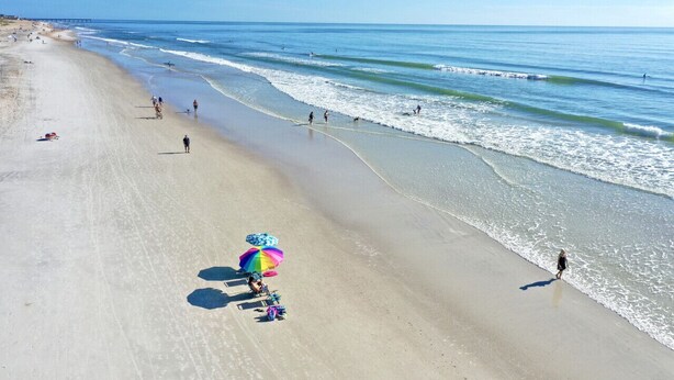 A beach with a clear sky, a pier in the distance, and people walking along the shore. - Ocean Song – Large 2 Bedroom with Private Ocean View Balcony & Sea Breezes & Pool Access (St. Augustine)
