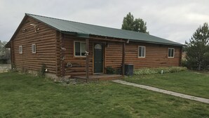 Una cabaña de troncos con puerta verde, un porche pequeño y techo de metal.