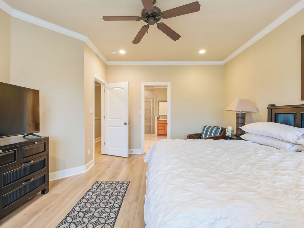 A bedroom with a bed, a ceiling fan, a TV, a dresser, and a patterned rug.