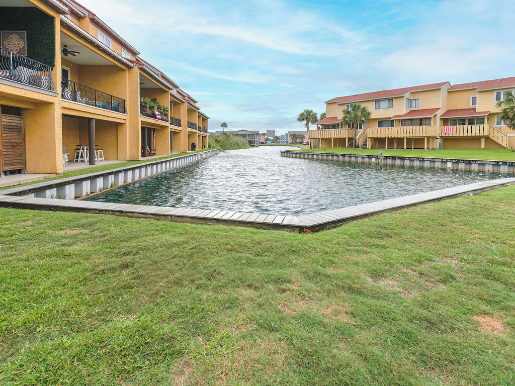 A waterway between two buildings with balconies, a grassy area, and a clear sky.