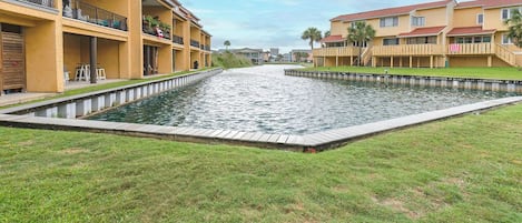 A waterway between two buildings with balconies, a grassy area, and a clear sky.