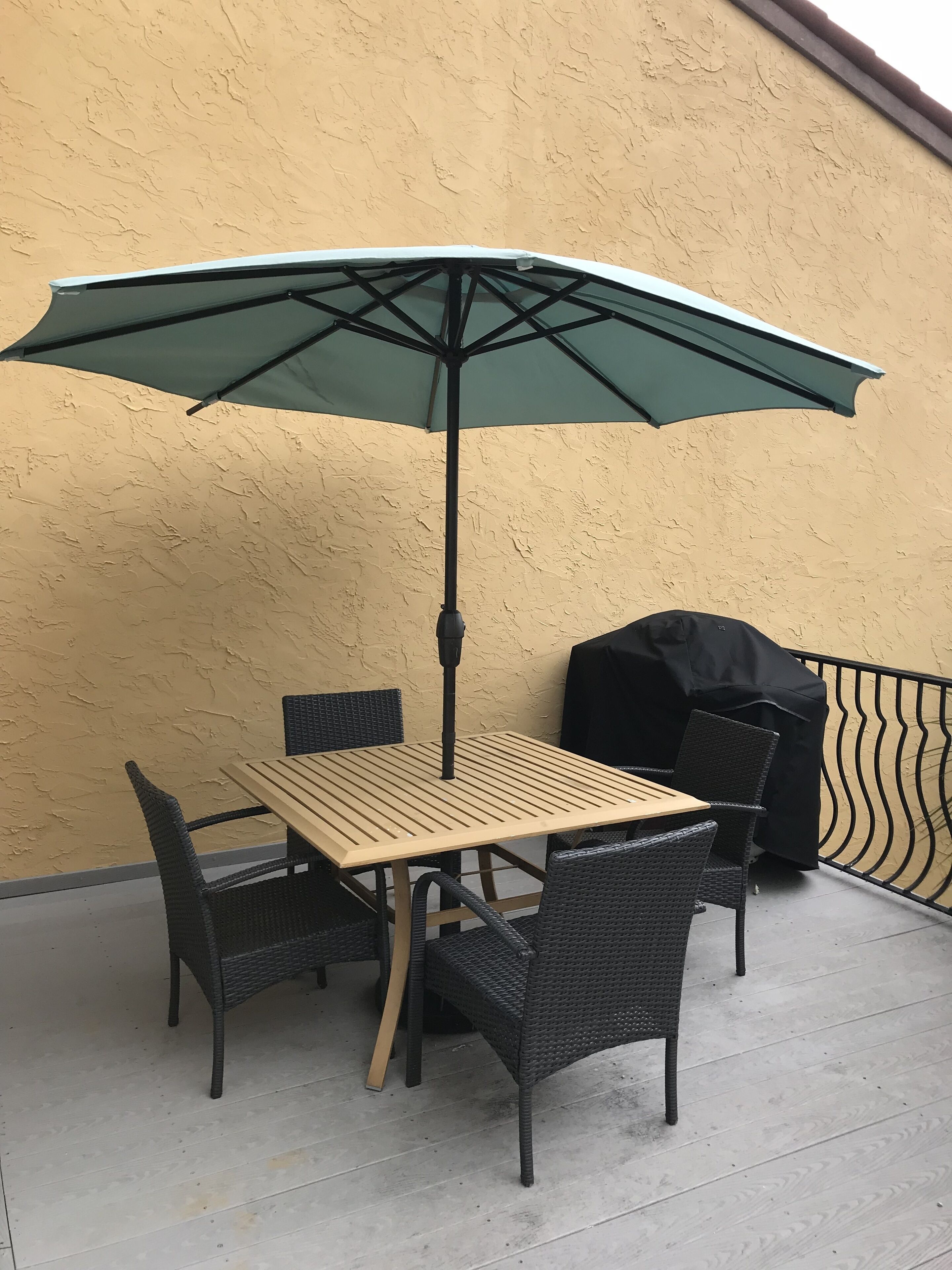 Un patio con una mesa, sillas, una sombrilla verde y una parrilla.