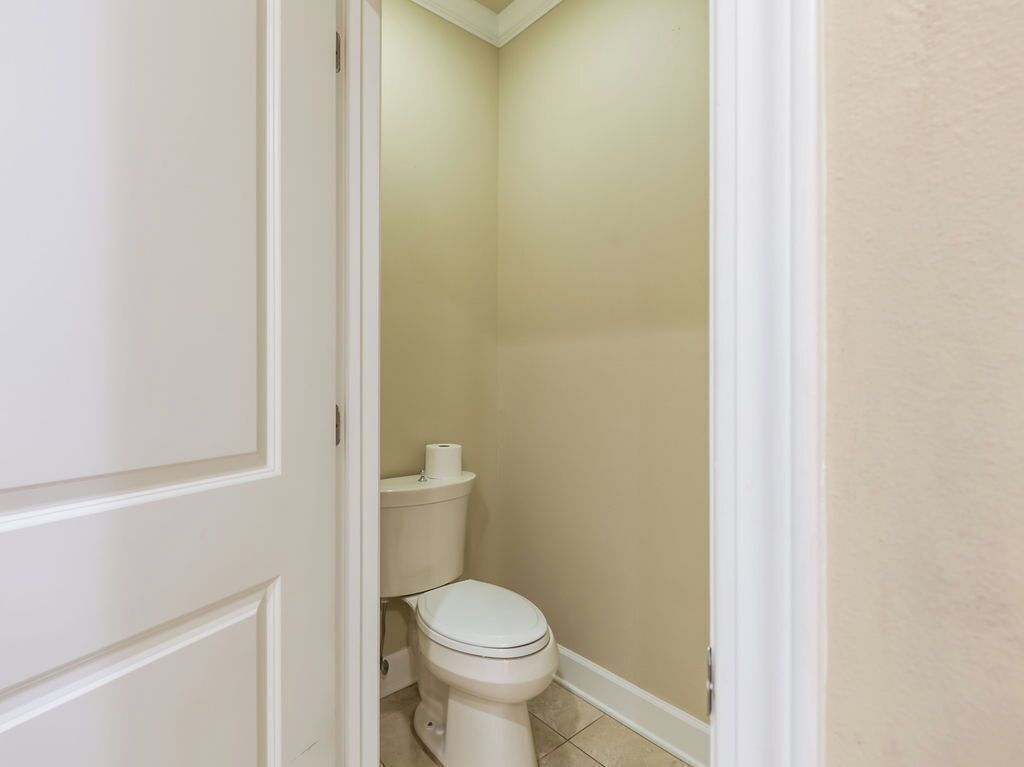 Une petite salle de bain étroite, avec des toilettes, un rouleau de papier toilette et une porte blanche.