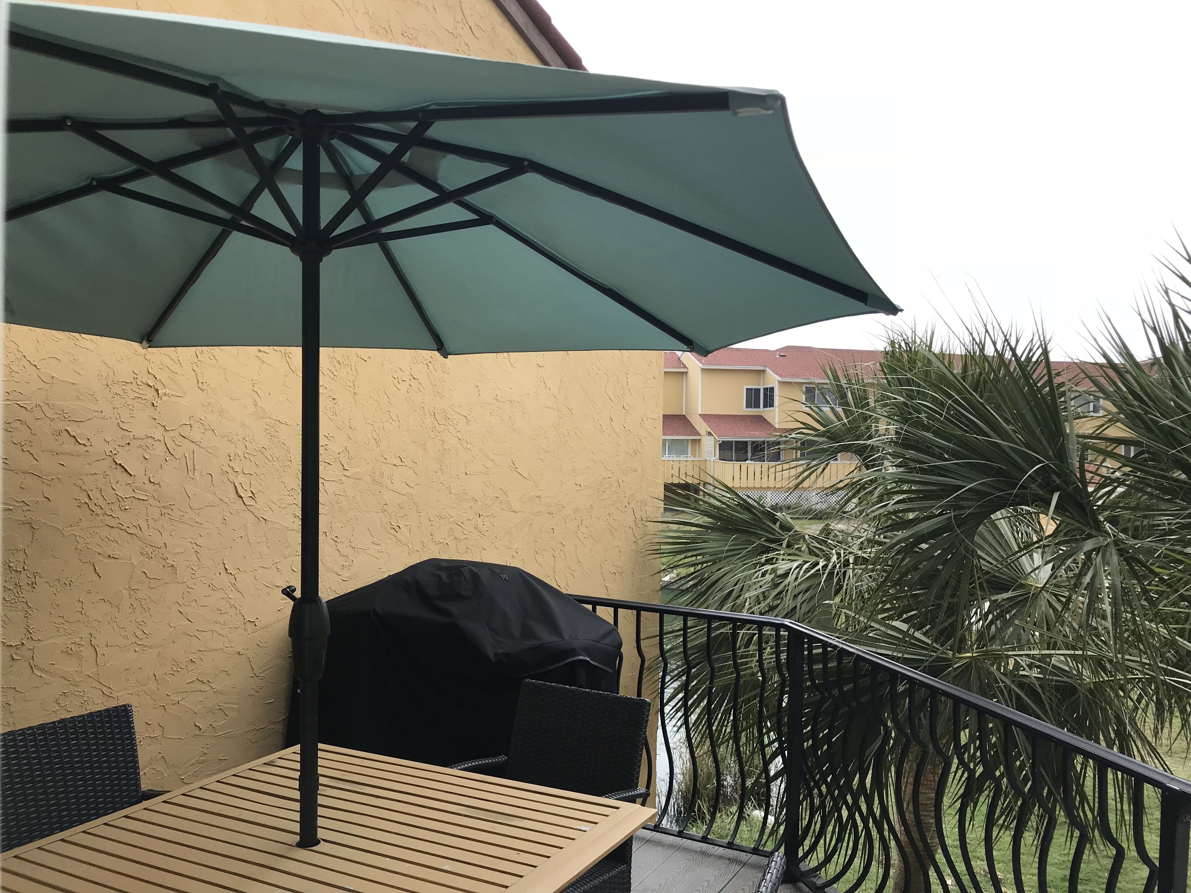 Een balkon met een tafel, stoelen, een groene parasol en een barbecue.