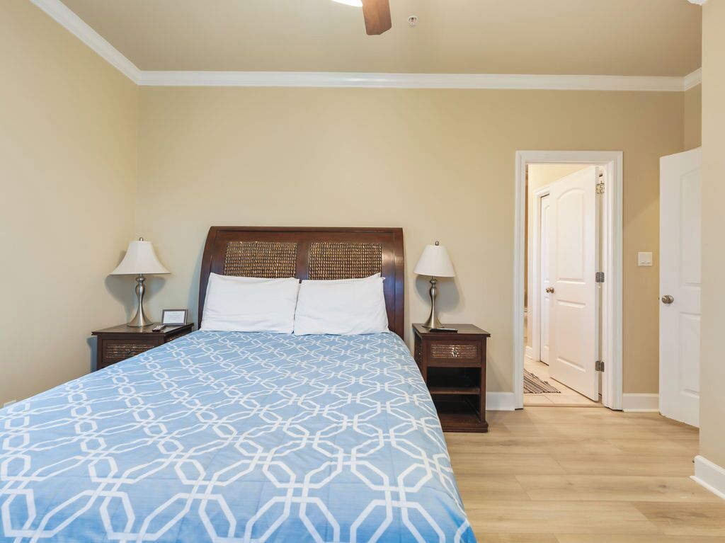 Une chambre à coucher comprenant un lit, deux tables de chevet, une commode, une porte et un ventilateur de plafond.