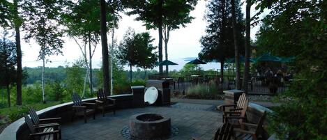 An outdoor seating area with a circular fire pit, wooden chairs, and tables.