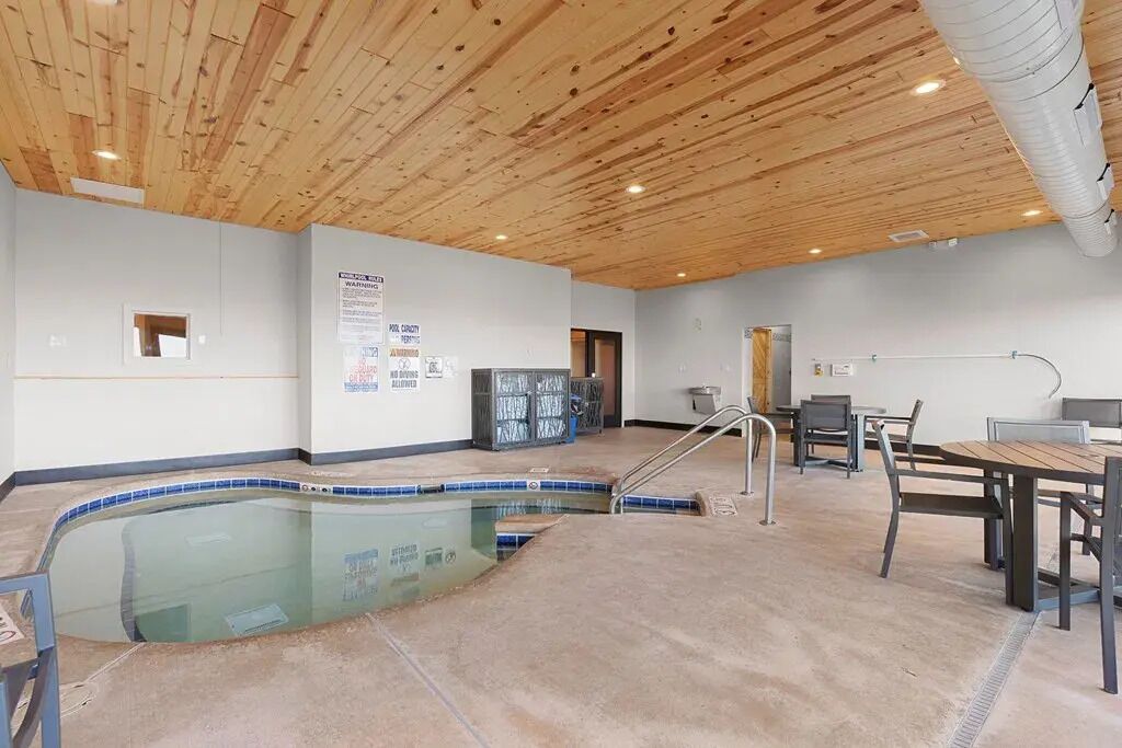 A pool area with a wooden ceiling, a pool, and a table with chairs.