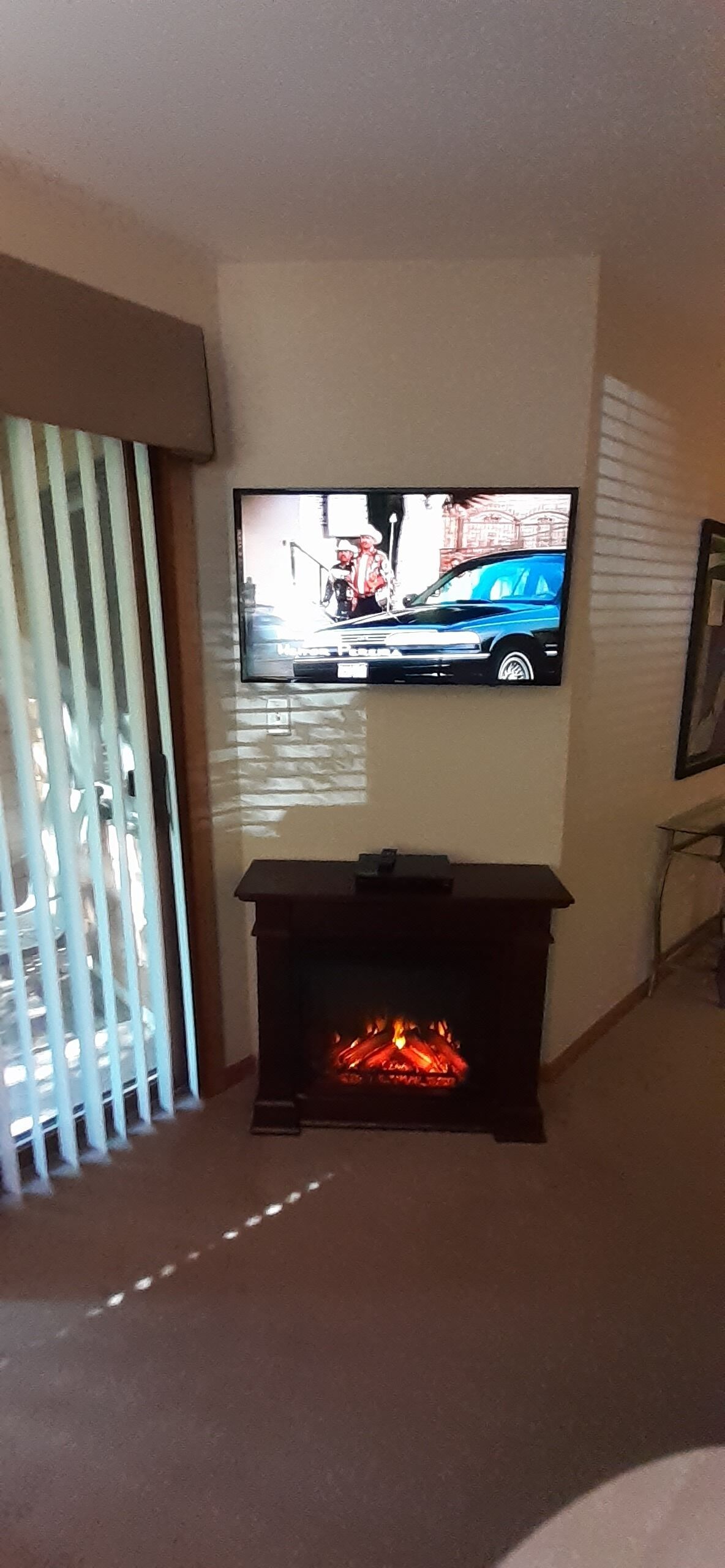 Un salón con televisión de pantalla plana en la pared, chimenea encendida y ventana con persianas.