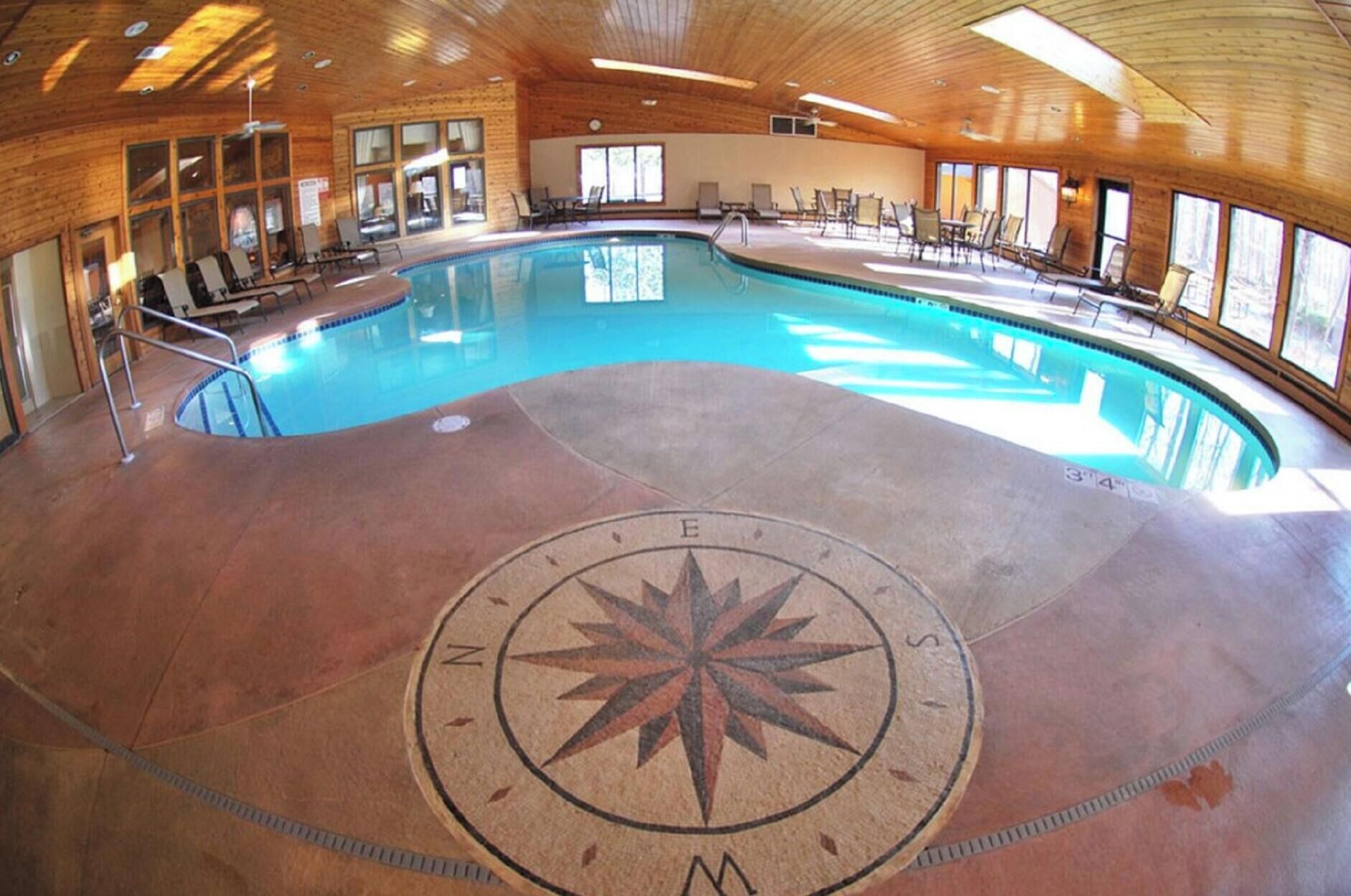 A large indoor pool with a compass design on the floor, surrounded by wooden walls and large windows.