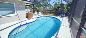 Una piscina con una zona de estar hundida, rodeada por un porche cubierto con sillas y una mesa.