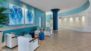 Un hall d’entrée aux murs de couleur turquoise, agrémenté d’œuvres d’art abstraites, de coins salon et d’un comptoir d’accueil.