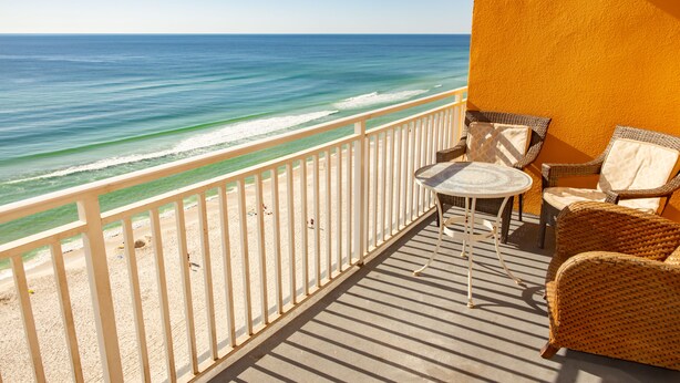 Un balcon avec vue sur l’océan, une petite table et des chaises en osier.