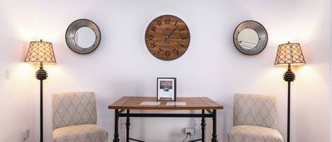 Une pièce comprenant une table en bois, deux chaises à motifs, une horloge murale, deux miroirs et deux lampadaires.