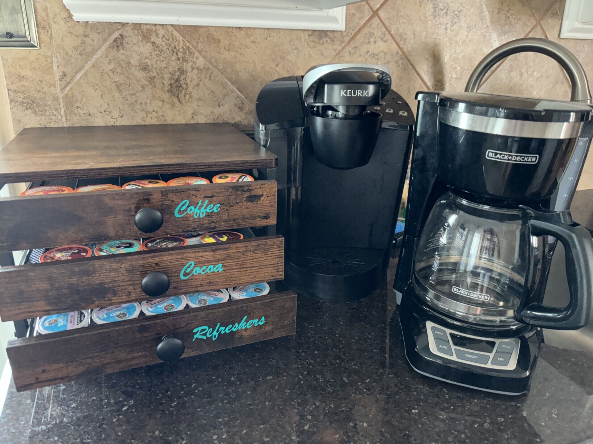 A coffee maker and a wooden coffee storage unit with compartments labeled 'Coffee,' 'Cocoa,' and 'Refreshers.'