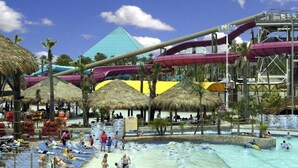 Un parque acuático con una piscina grande, toboganes de agua y sombrillas de paja.