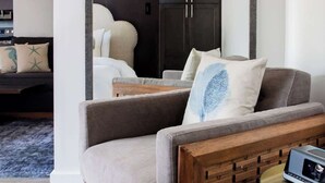 Un salon moderne avec un canapé gris, une table d’appoint en bois et une petite table ronde sur laquelle se trouve un ordinateur portable.
