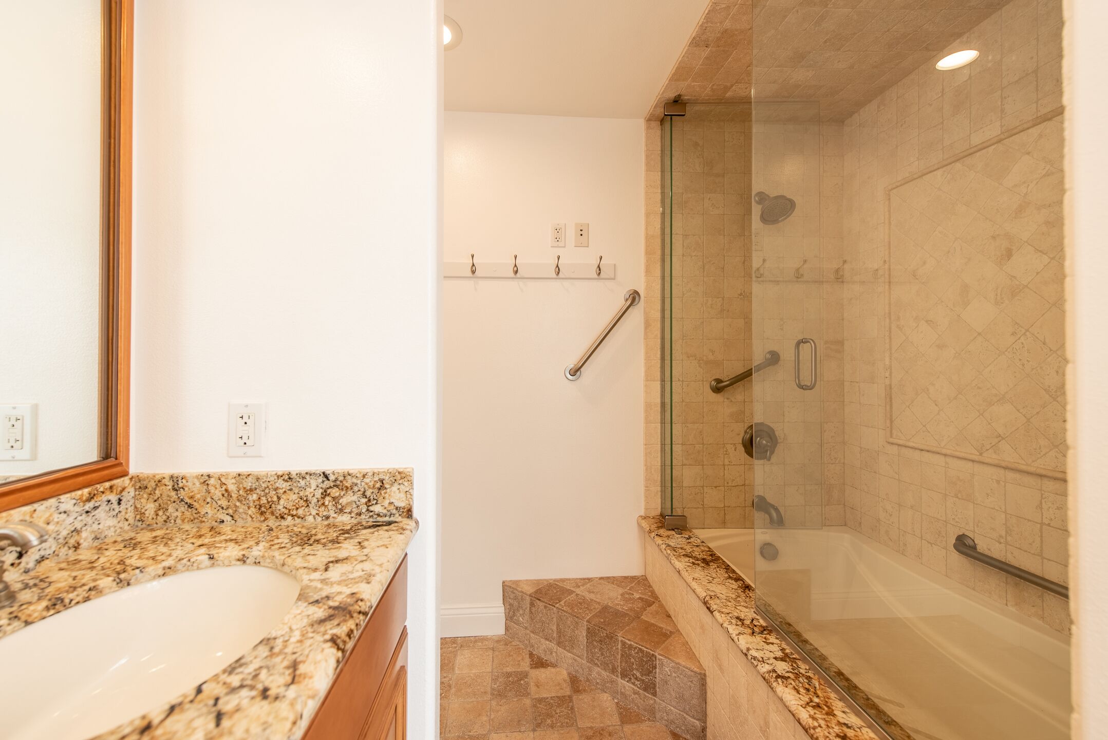 Baño con lavamanos de encimera de granito, cabina de ducha con paredes de vidrio y zona de ducha con azulejos de mármol.