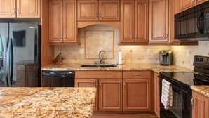 Eine Küche mit Holzschränken, einer Granit Arbeitsplatte, einem Edelstahl Kühlschrank, einer Mikrowelle und einem Geschirrspüler.