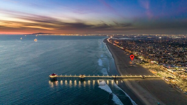 Luftaufnahme einer Küstenstadt mit einer langen Mole, die sich ins Meer erstreckt, einem Strand und einem dicht besiedelten Gebiet mit Beleuchtung.