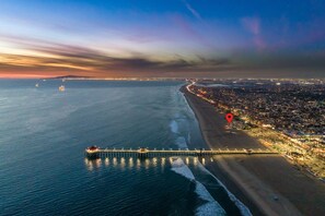 An aerial view of a coastal city with a long pier extending into the sea, a beach, and a densely populated area with lights.