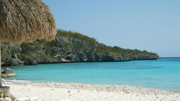 A beach with white lounge chairs and a thatched umbrella. - PREMIER HOST Private 3 bdrm, 1600 sq ft Fully Air-Conditioned villa in Blue Bay (Sint Michiel)