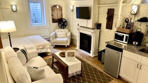 A modern living room with a fireplace, a television, and a kitchen area with a microwave and coffee maker. - Charming Studio in Heart of City Park--Minutes to downtown!! MANY AMENITIES!! (Denver)