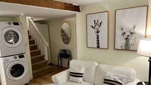 A living room with a sofa, two framed animal portraits, a washing machine, and a staircase. - Charming Studio in Heart of City Park--Minutes to downtown!! MANY AMENITIES!! (Denver)