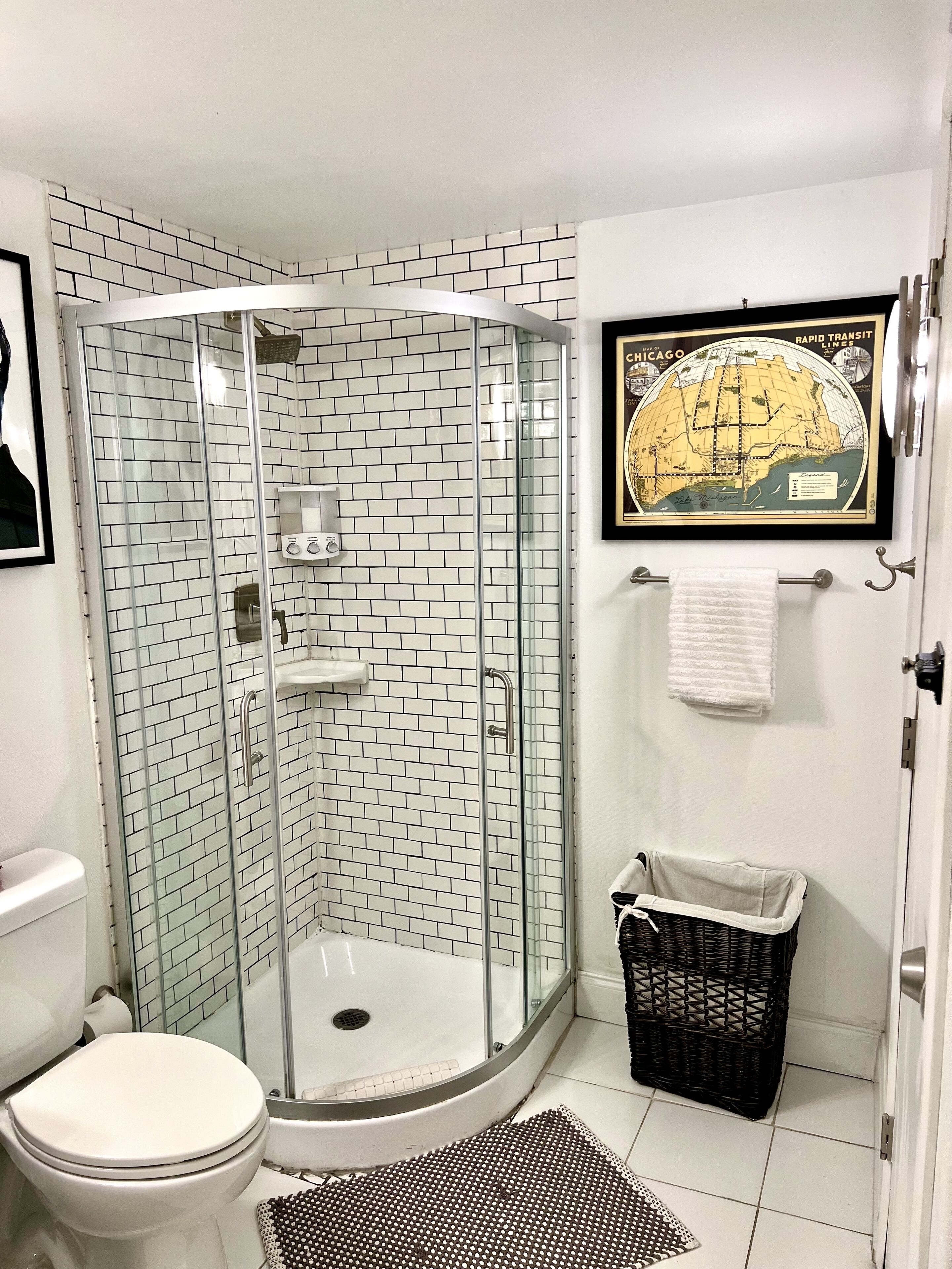 A bathroom with a glass-enclosed shower, a toilet, a sink, and a framed map on the wall.