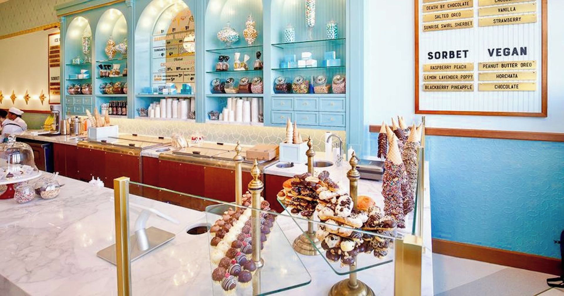 An ice cream parlor with a variety of ice cream flavors and sorbets displayed on shelves and a menu board.
