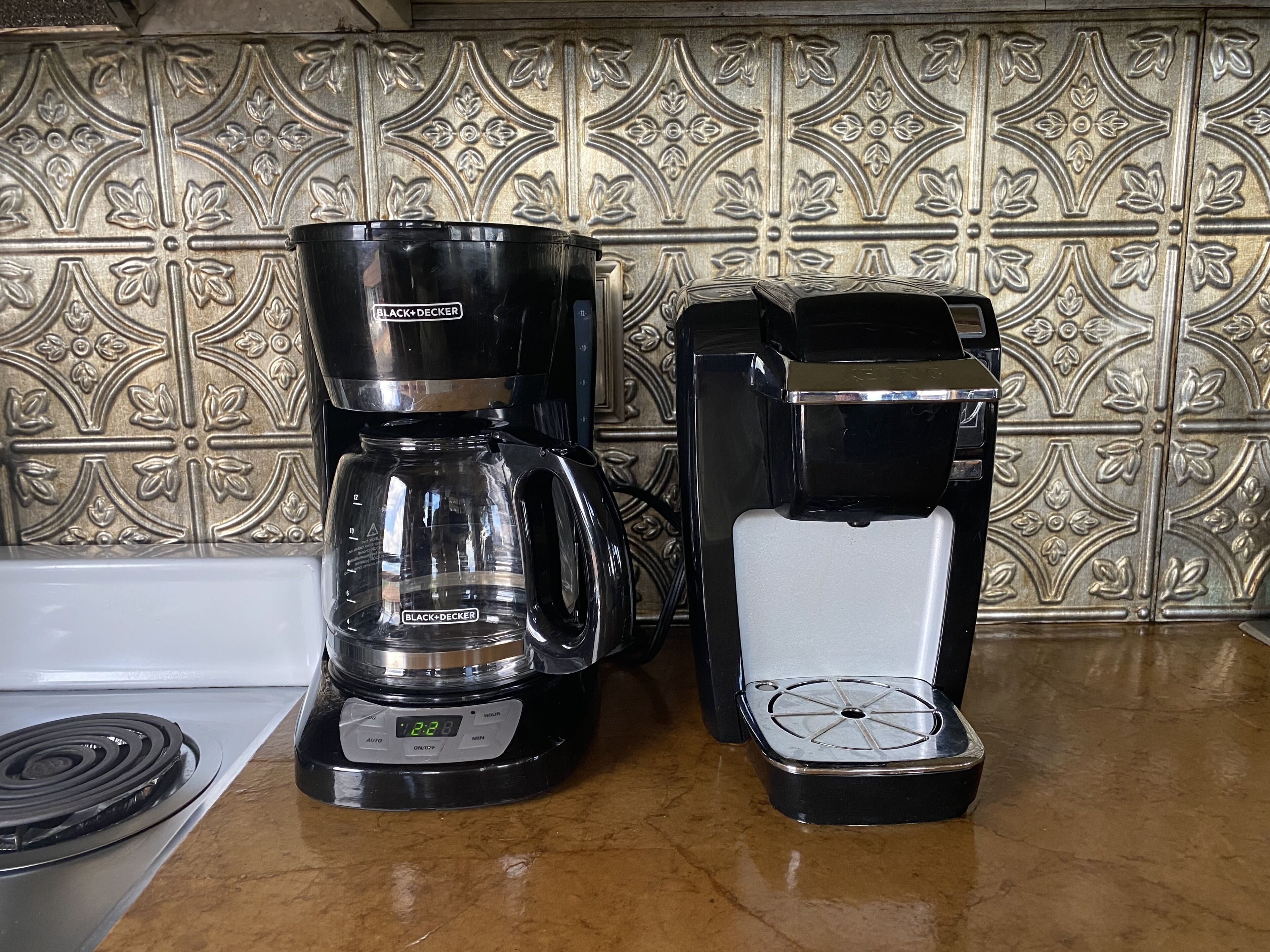 Two coffee makers on a kitchen counter with a decorative backsplash.