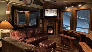 A cozy living room with a fireplace, leather sofa, wooden benches, and large windows with a snowy view.