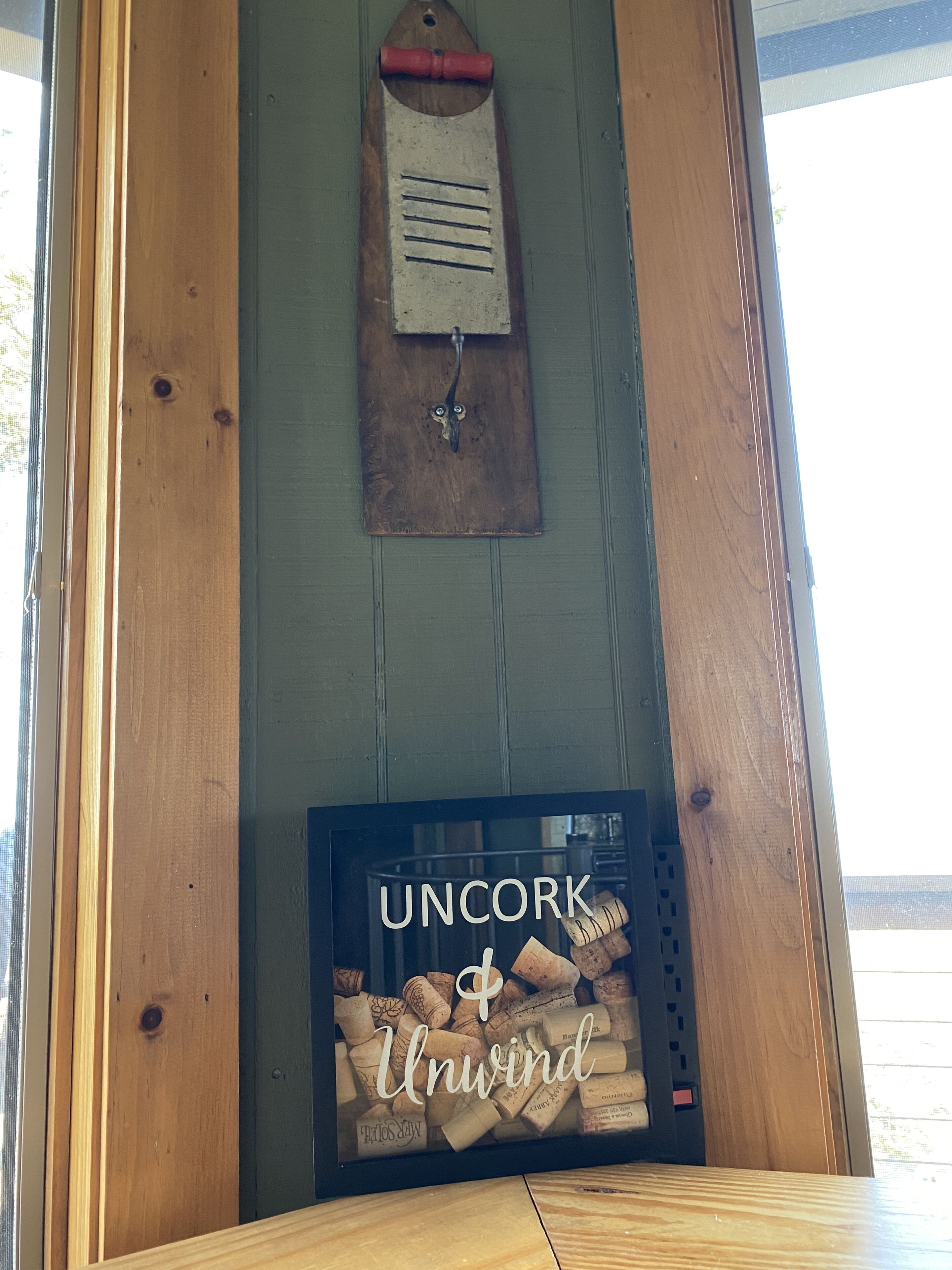 A wooden wall with a cork and wine rack, and a framed sign with 'Uncork & Unwind' text.