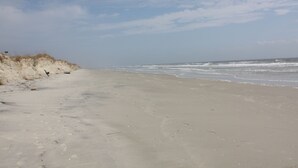 Een zanderig strand met voetafdrukken en weinig begroeiing.