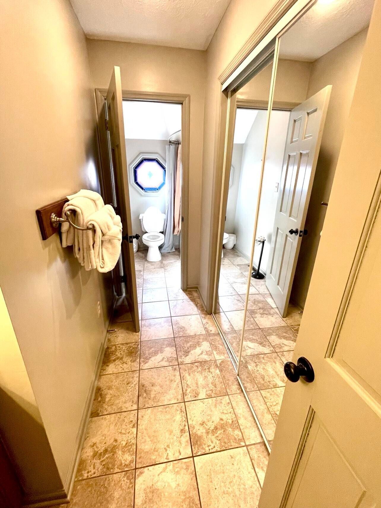 A hallway with a tiled floor leading to a bathroom with a toilet and a window.