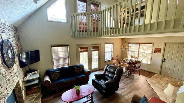 A spacious living area with a high ceiling, a stone fireplace, a large window, and a balcony with a railing. - 3 BR/3BATH Retreat 1.5 miles from Attraction/Resort Pool/Pool Table/Arcade (Pigeon Forge)