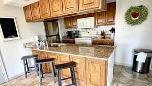 A kitchen with wooden cabinets, a granite countertop, and two bar stools. - 3 BR/3BATH Retreat 1.5 miles from Attraction/Resort Pool/Pool Table/Arcade (Pigeon Forge)