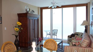 Ein Wohnzimmer mit Glastisch, Stühlen, einer Couch, einer Holzkommode und einem großen Fenster mit Ausblick.