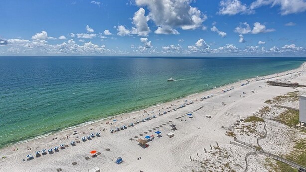 Ein Strand mit Reihen von Sonnenschirmen und Liegestühlen, einem klaren Himmel und dem Meer.
