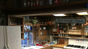Une cuisine rustique avec des armoires en bois, un réfrigérateur blanc et une cuisinière. Une pancarte sur laquelle on peut lire « On n’en a jamais assez » est accrochée au-dessus de la cuisinière.